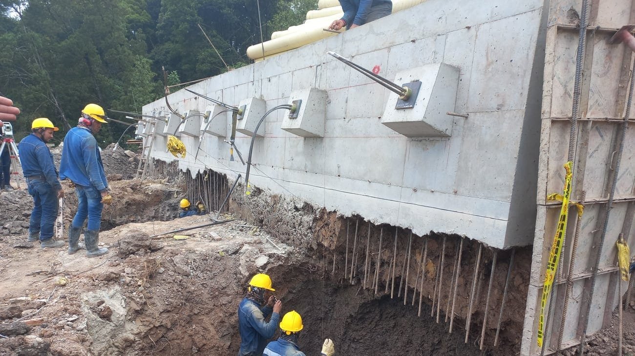 Pantalla anclada en ejecución sobre ladera urbana, con cuadrilla instalando los anclajes